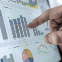 A person is pointing at a computer screen with graphs on it - representing Optimum Transitions' core value of driving forward with innovation