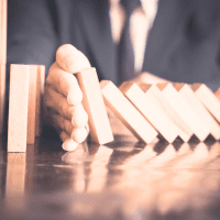 a person in a suit and tie sticks his hand out to protect dominoes from falling down - representing Optimum Transitions' core value of protecting legacies